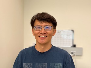 professor wearing a blue shirt in front of a tan backdrop